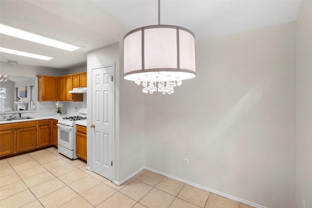 kitchen with decorative backsplash, light tile patterned floors, white gas stove, a notable chandelier, and sink