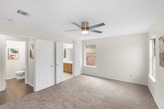 unfurnished bedroom featuring ensuite bathroom, light colored carpet, and ceiling fan