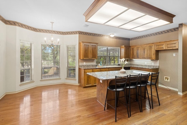 kitchen featuring light stone countertops, light wood-type flooring, a center island, pendant lighting, and an inviting chandelier