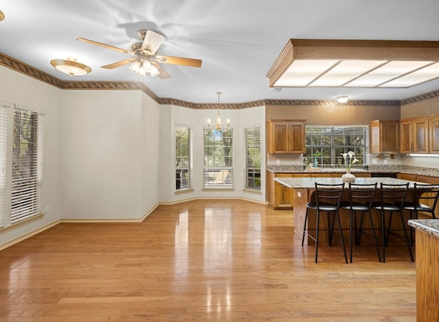 kitchen with a kitchen breakfast bar, ceiling fan with notable chandelier, pendant lighting, and light hardwood / wood-style floors