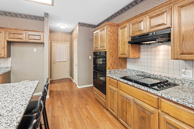 kitchen with light stone counters, decorative backsplash, black appliances, and light wood-type flooring