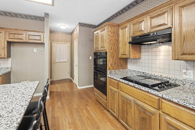 300 Delaware Springs Blvd, Burnet, TX 78611 - kitchen featuring under cabinet range hood, black appliances, wallpapered walls, light wood-style flooring, and decorative backsplash