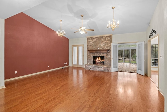 unfurnished living room with high vaulted ceiling, wood-type flooring, a brick fireplace, and ceiling fan with notable chandelier