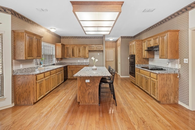 kitchen featuring a breakfast bar area, sink, a center island, light wood-type flooring, and light stone counters