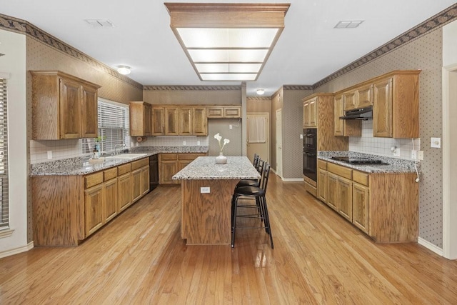 300 Delaware Springs Blvd, Burnet, TX 78611 - kitchen featuring light wood-style floors, wallpapered walls, a center island, under cabinet range hood, and a breakfast bar area