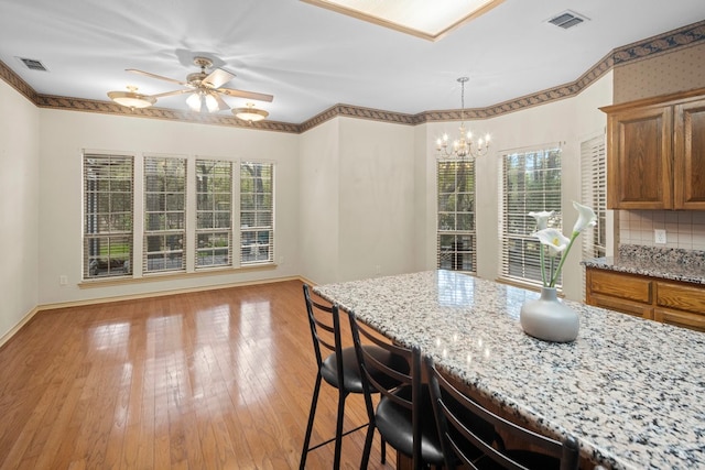 kitchen with light stone countertops, light hardwood / wood-style flooring, ceiling fan with notable chandelier, and plenty of natural light