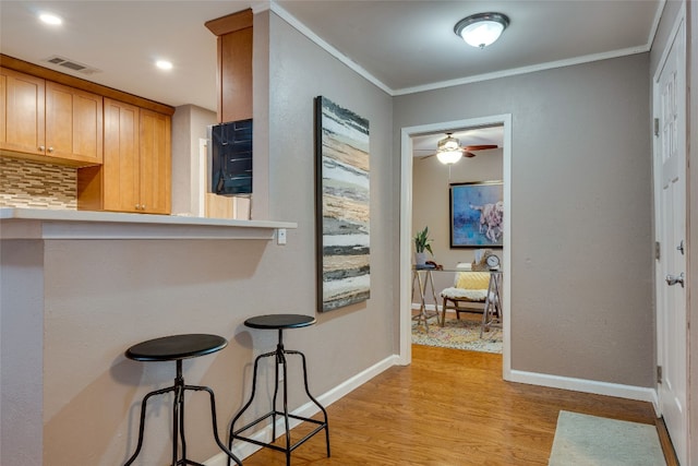 kitchen with backsplash, crown molding, light hardwood / wood-style floors, and ceiling fan