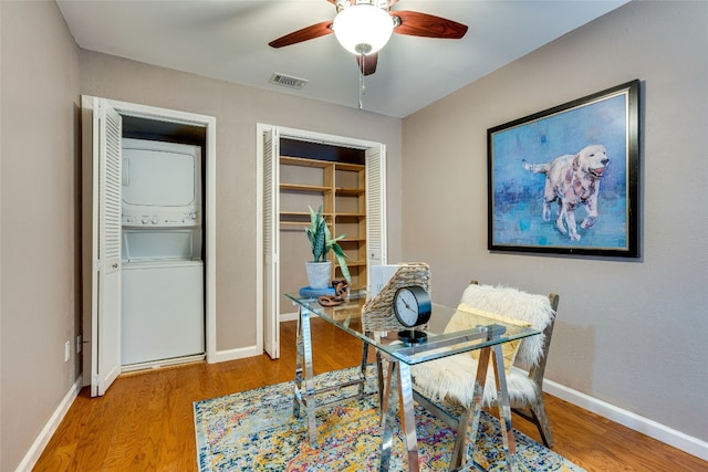 office space featuring stacked washer and dryer, wood-type flooring, and ceiling fan