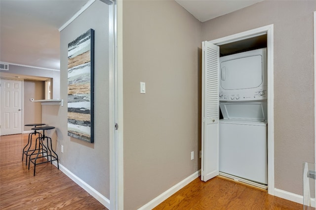 clothes washing area featuring crown molding, hardwood / wood-style floors, and stacked washer / drying machine