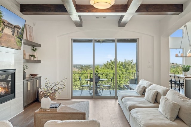 living room with beam ceiling, hardwood / wood-style floors, and a tiled fireplace