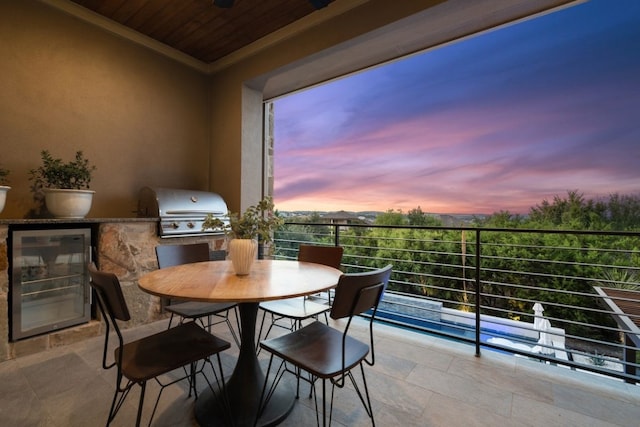 balcony at dusk featuring exterior kitchen, area for grilling, and beverage cooler