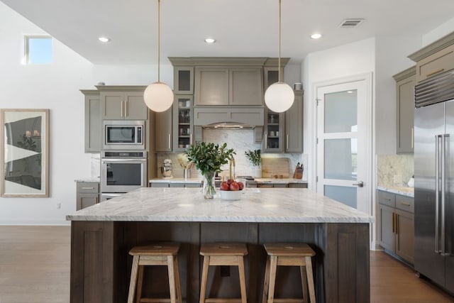 kitchen with built in appliances, backsplash, pendant lighting, and a kitchen island