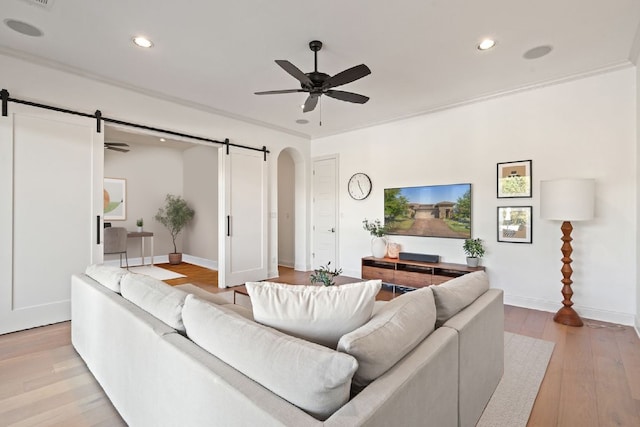 living room featuring ceiling fan, crown molding, light wood-type flooring, and a barn door