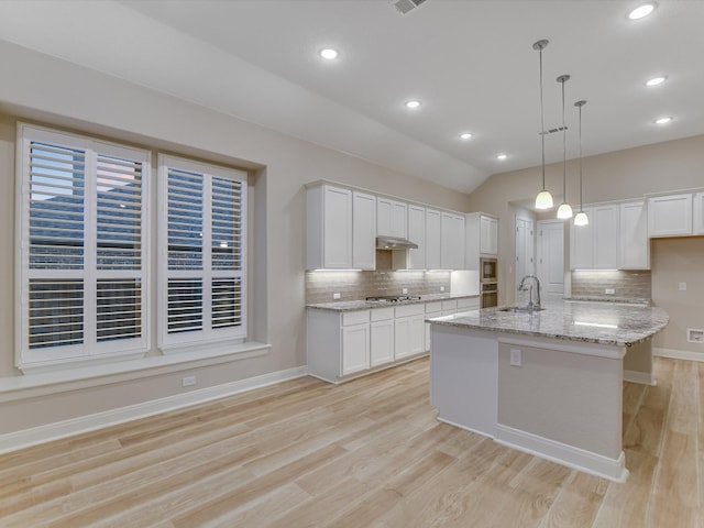 kitchen featuring white cabinets, hanging light fixtures, light wood-type flooring, and an island with sink