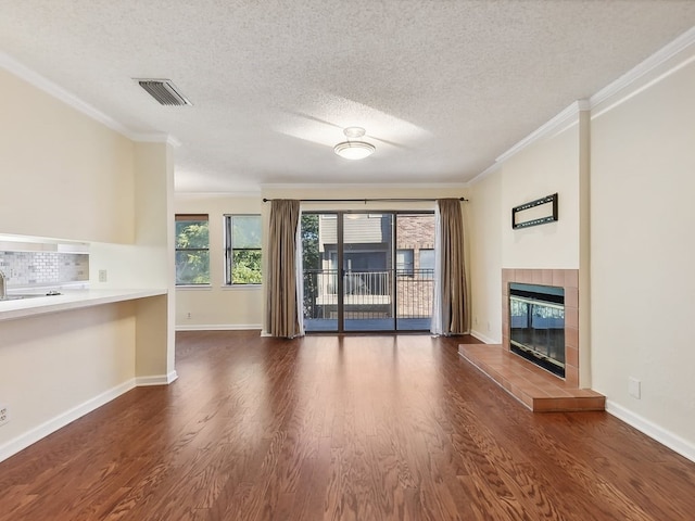 unfurnished living room featuring crown molding, a textured ceiling, a tile fireplace, and dark hardwood / wood-style flooring