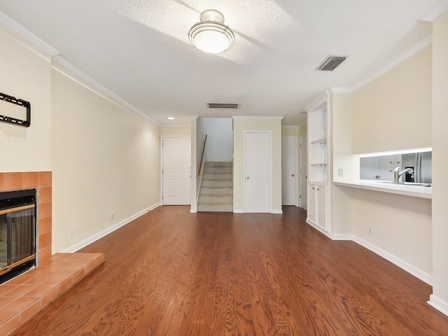 unfurnished living room featuring a textured ceiling, ornamental molding, dark hardwood / wood-style flooring, and a tile fireplace