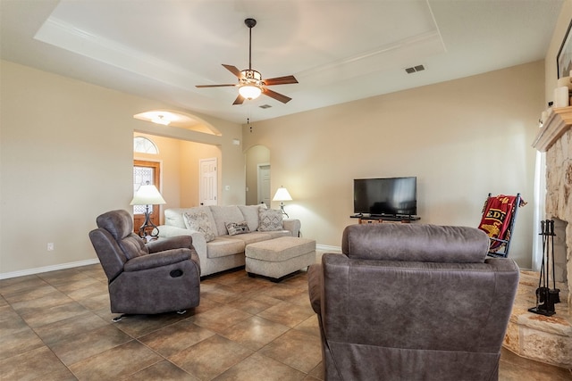 living room with ceiling fan, a tray ceiling, and a fireplace