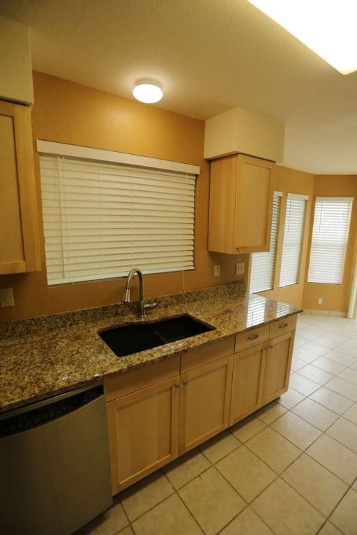 kitchen with light brown cabinets, dishwasher, sink, and light tile patterned floors