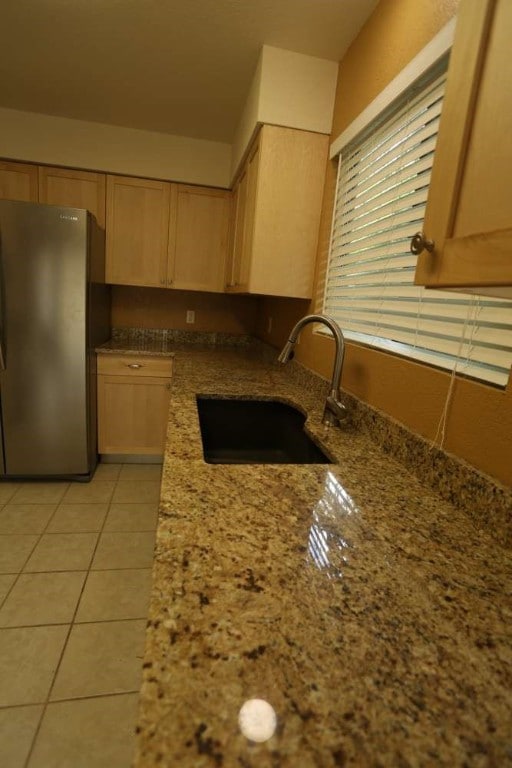 kitchen with light brown cabinetry, sink, stainless steel fridge, light stone counters, and light tile patterned floors