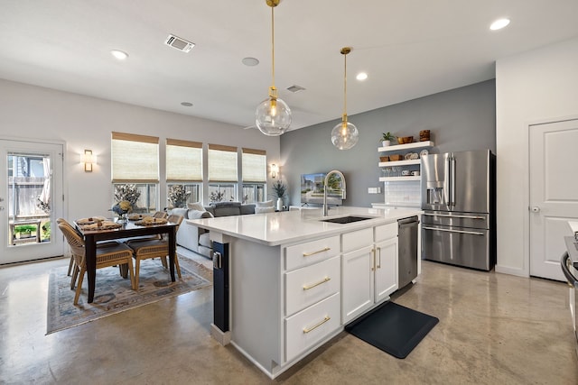 kitchen featuring appliances with stainless steel finishes, decorative light fixtures, white cabinetry, sink, and a kitchen island with sink