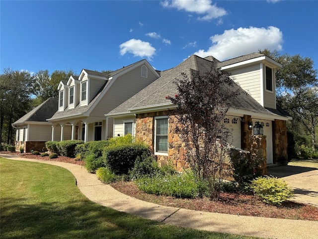 view of property exterior with driveway, a garage, stone siding, roof with shingles, and a yard