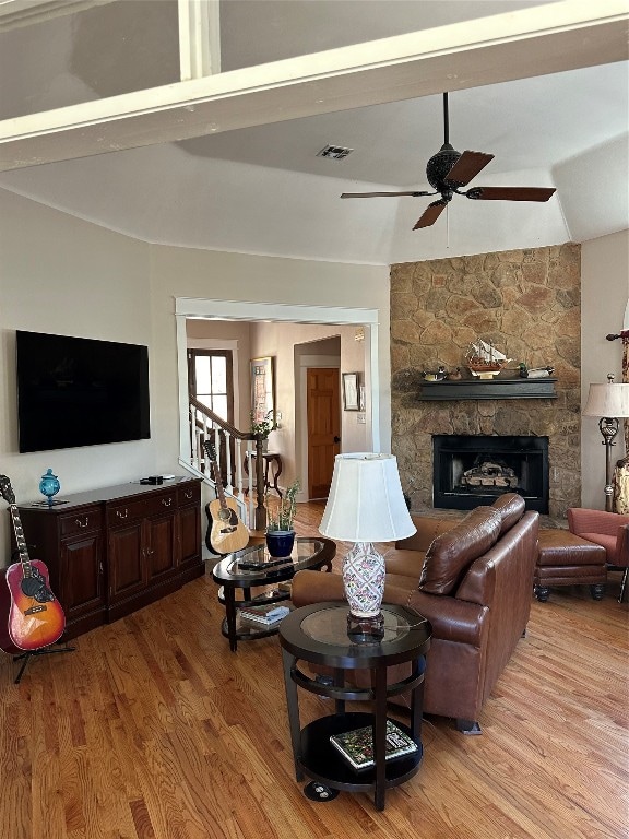 living room featuring a fireplace, ceiling fan, light wood-type flooring, and vaulted ceiling