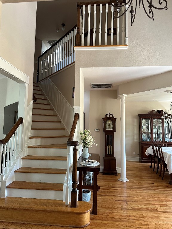 staircase featuring ornate columns, hardwood / wood-style flooring, a chandelier, and a high ceiling