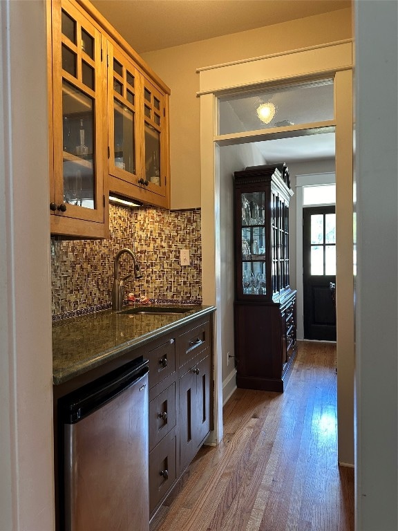 bar with sink, backsplash, stainless steel fridge, dark stone counters, and dark wood-type flooring