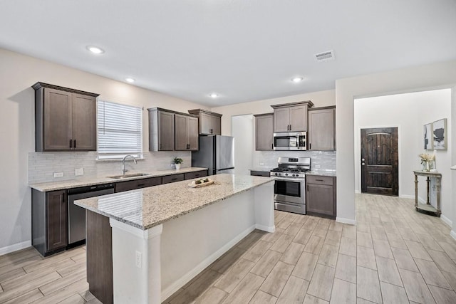 309 Greenway Dr, Georgetown, TX 78628 - kitchen with stainless steel appliances, light wood finished floors, a kitchen island, backsplash, and dark brown cabinetry