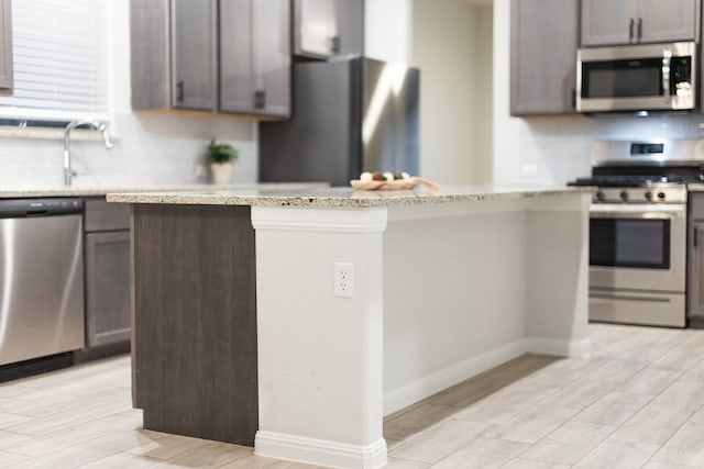 kitchen featuring light stone countertops, dark brown cabinetry, appliances with stainless steel finishes, and light hardwood / wood-style flooring