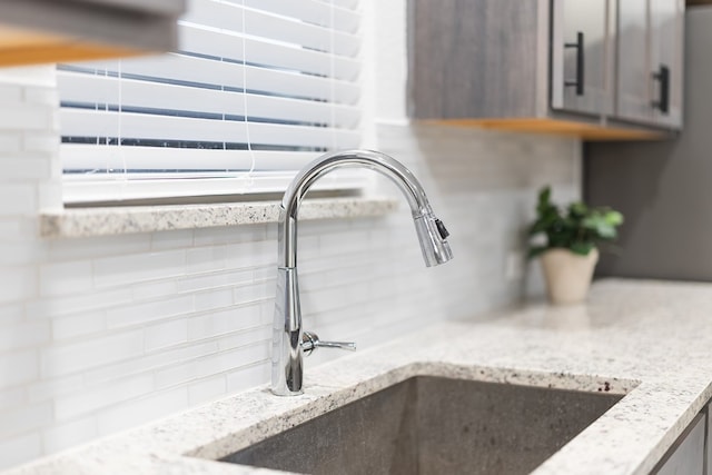 room details featuring sink, light stone countertops, and tasteful backsplash