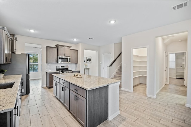 kitchen with light stone countertops, a kitchen island, appliances with stainless steel finishes, and light hardwood / wood-style floors