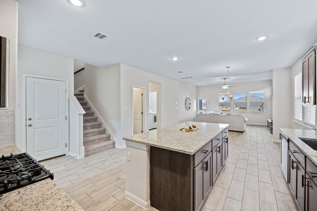 kitchen with a kitchen island, dark brown cabinetry, stainless steel dishwasher, light stone counters, and light hardwood / wood-style flooring