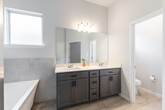 bathroom featuring toilet, plenty of natural light, vanity, and a bath