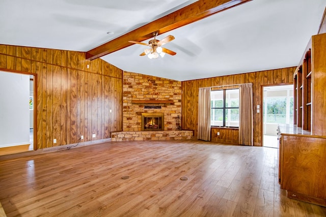 unfurnished living room featuring wood walls, lofted ceiling with beams, a stone fireplace, ceiling fan, and light hardwood / wood-style floors