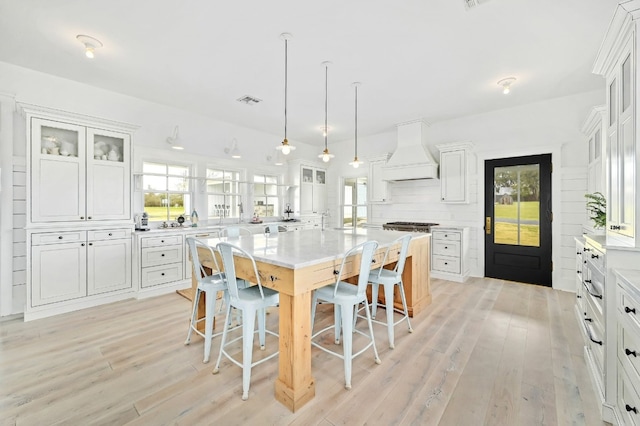 kitchen featuring custom exhaust hood, white cabinets, light hardwood / wood-style flooring, decorative light fixtures, and a center island