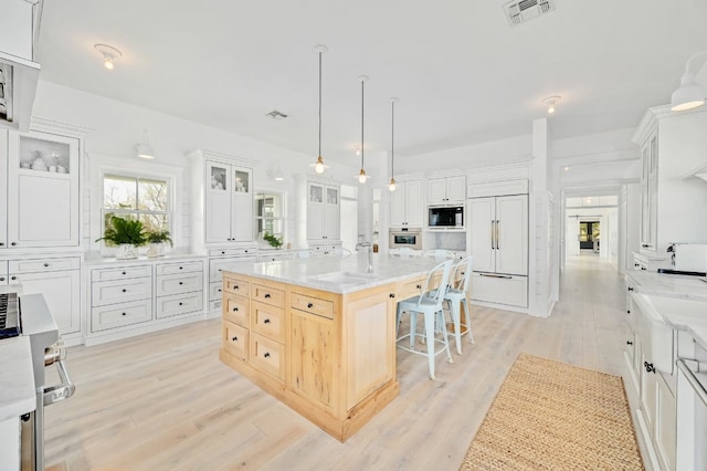 kitchen featuring a kitchen island, white cabinetry, built in appliances, pendant lighting, and light hardwood / wood-style floors