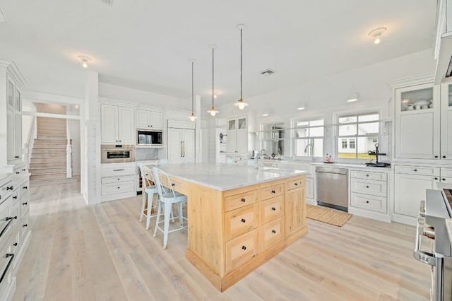233 W Mill St, Round Top, TX 78954 - kitchen featuring appliances with stainless steel finishes, a kitchen bar, a large island with sink, light wood-type flooring, and glass insert cabinets