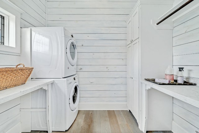 washroom with light hardwood / wood-style floors, stacked washing maching and dryer, and wooden walls