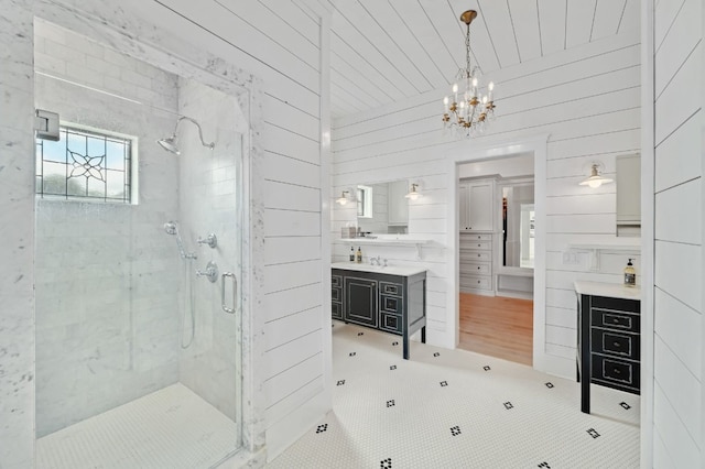 bathroom with tile patterned flooring, an inviting chandelier, walk in shower, vanity, and wood walls