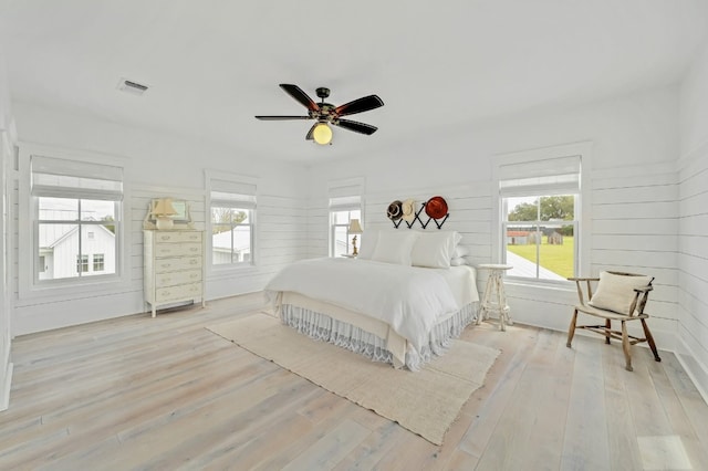 bedroom with wood walls, multiple windows, light hardwood / wood-style floors, and ceiling fan