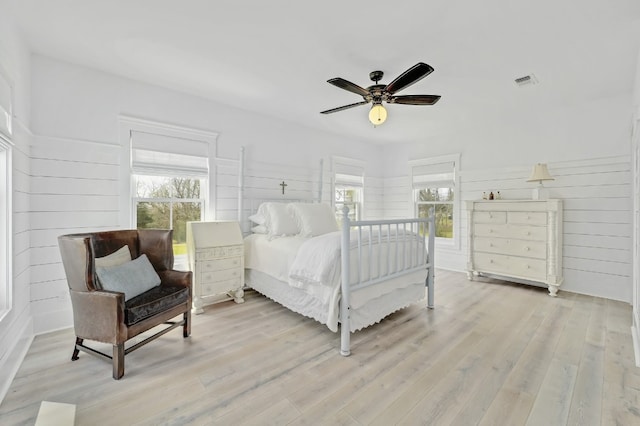 bedroom with wooden walls, light wood-type flooring, and ceiling fan