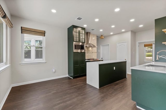 kitchen with stainless steel microwave, sink, wall chimney exhaust hood, dark wood-type flooring, and a kitchen island with sink