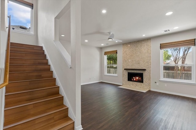 unfurnished living room featuring a large fireplace, ceiling fan, a healthy amount of sunlight, and dark hardwood / wood-style flooring