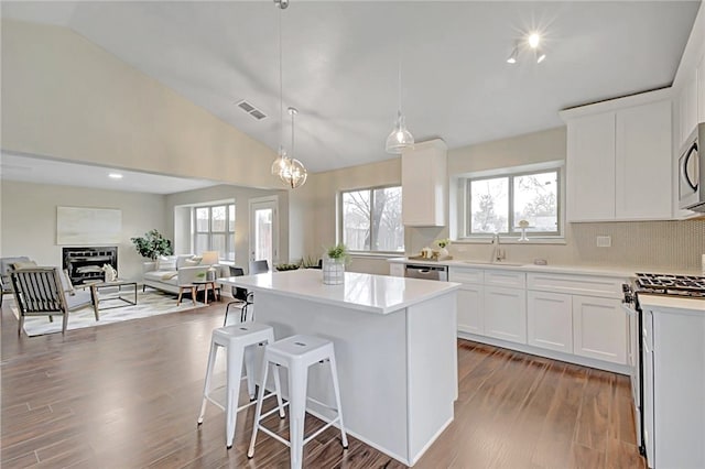 kitchen with white cabinets, stainless steel appliances, hardwood / wood-style floors, and pendant lighting