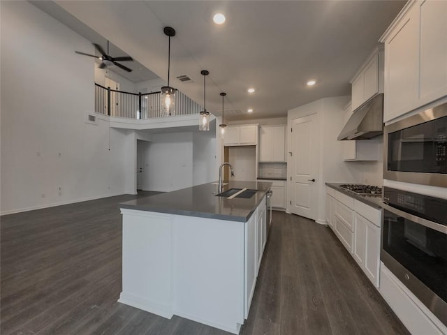 kitchen with dark countertops, under cabinet range hood, appliances with stainless steel finishes, dark wood-style floors, and a sink