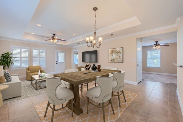 tiled dining space featuring ceiling fan with notable chandelier, a raised ceiling, and ornamental molding