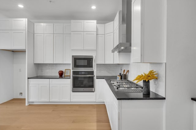 kitchen with white cabinets, wall chimney range hood, backsplash, light hardwood / wood-style floors, and stainless steel gas stovetop