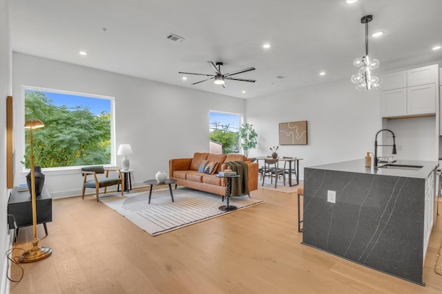 living room featuring light hardwood / wood-style floors, sink, and ceiling fan with notable chandelier