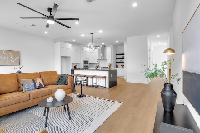 living room with sink, ceiling fan with notable chandelier, and light wood-type flooring